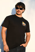 Model wearing a Common Saints black crew-neck T-shirt with small praying hands chest logo and “Saints of the Common Grind” text