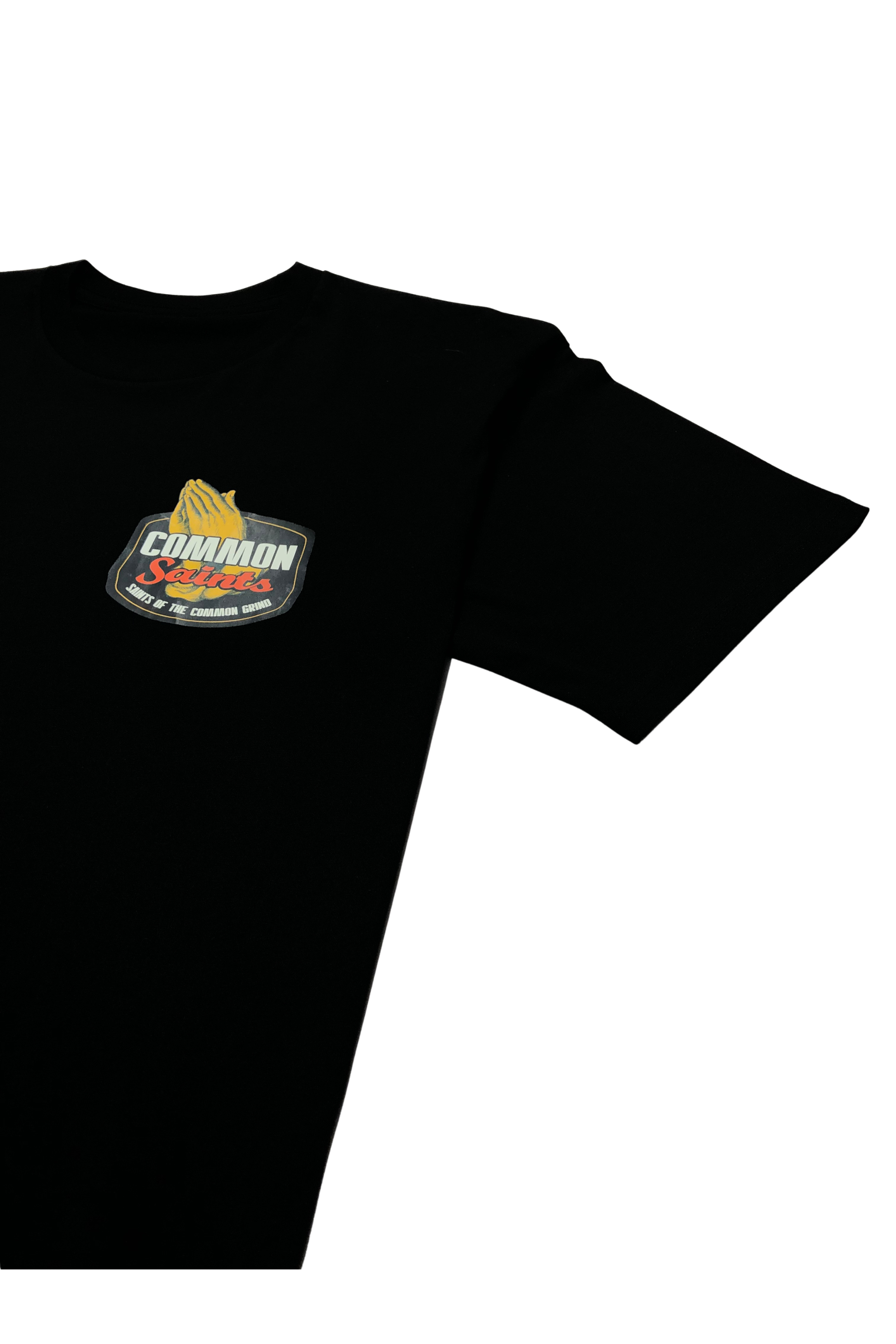 Close-up of the small Common Saints left-chest logo on a black T-shirt with praying hands and “Saints of the Common Grind” text