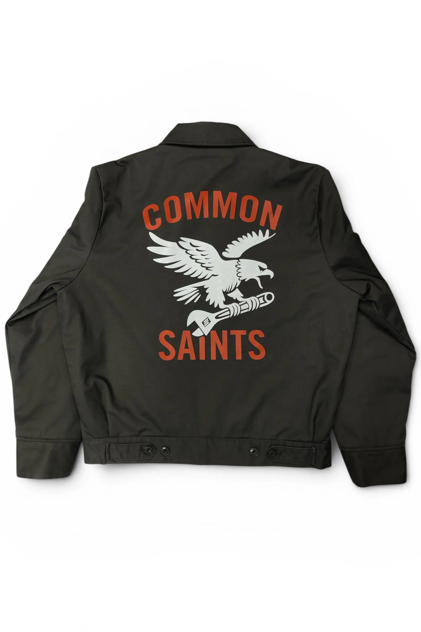 Common Saints dark gray mechanic jacket with large white eagle-and-wrench back graphic and red “Common Saints” lettering