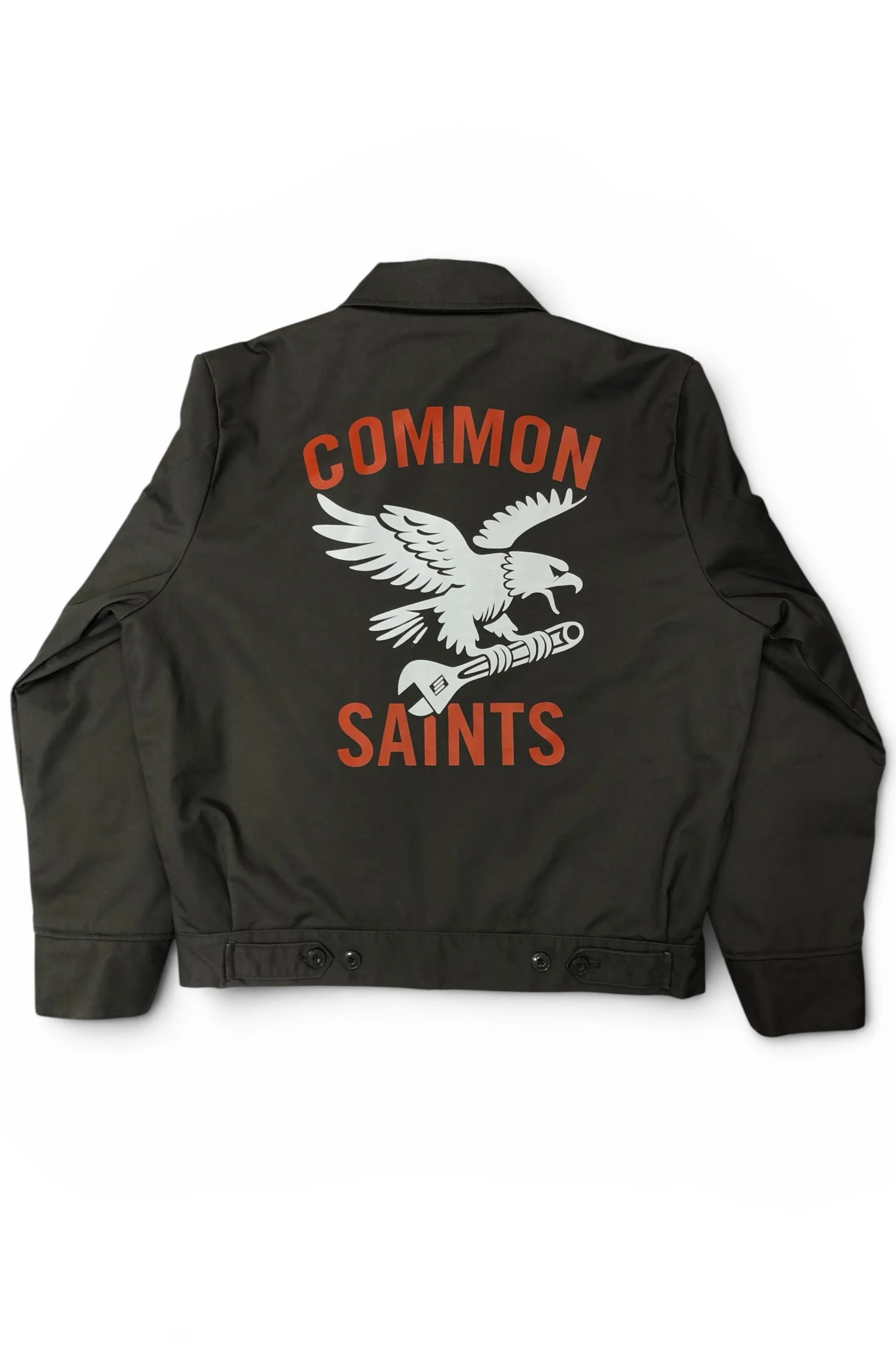 Common Saints dark gray mechanic jacket with large white eagle-and-wrench back graphic and red “Common Saints” lettering