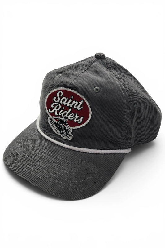 Angled view of the Common Saints dark gray corduroy rope cap with Saint Riders patch, skateboarder graphic, and curved brim