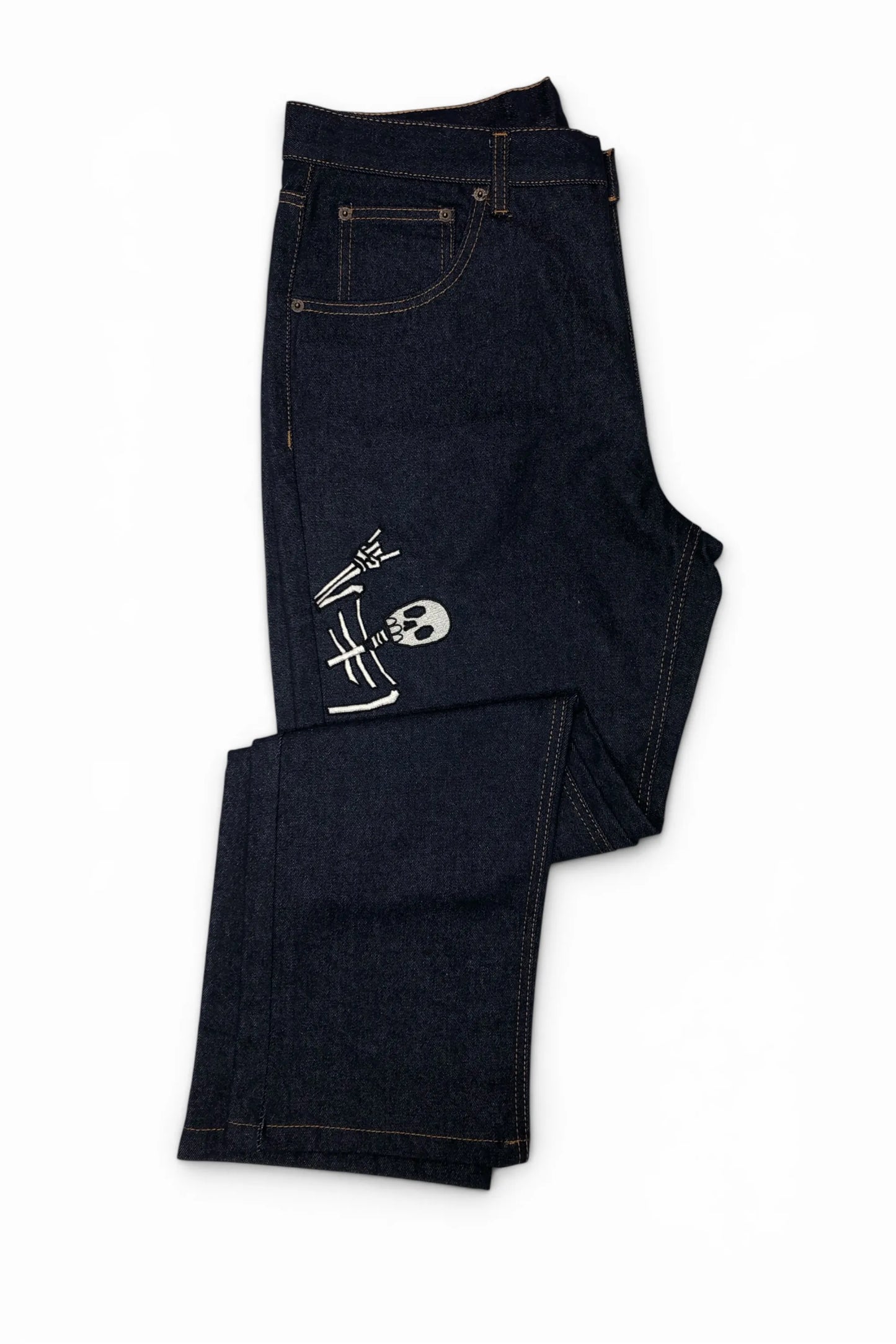 Common Saints dark indigo denim jeans with contrast stitching and white embroidered skull-and-bones graphic on the left thigh, folded view