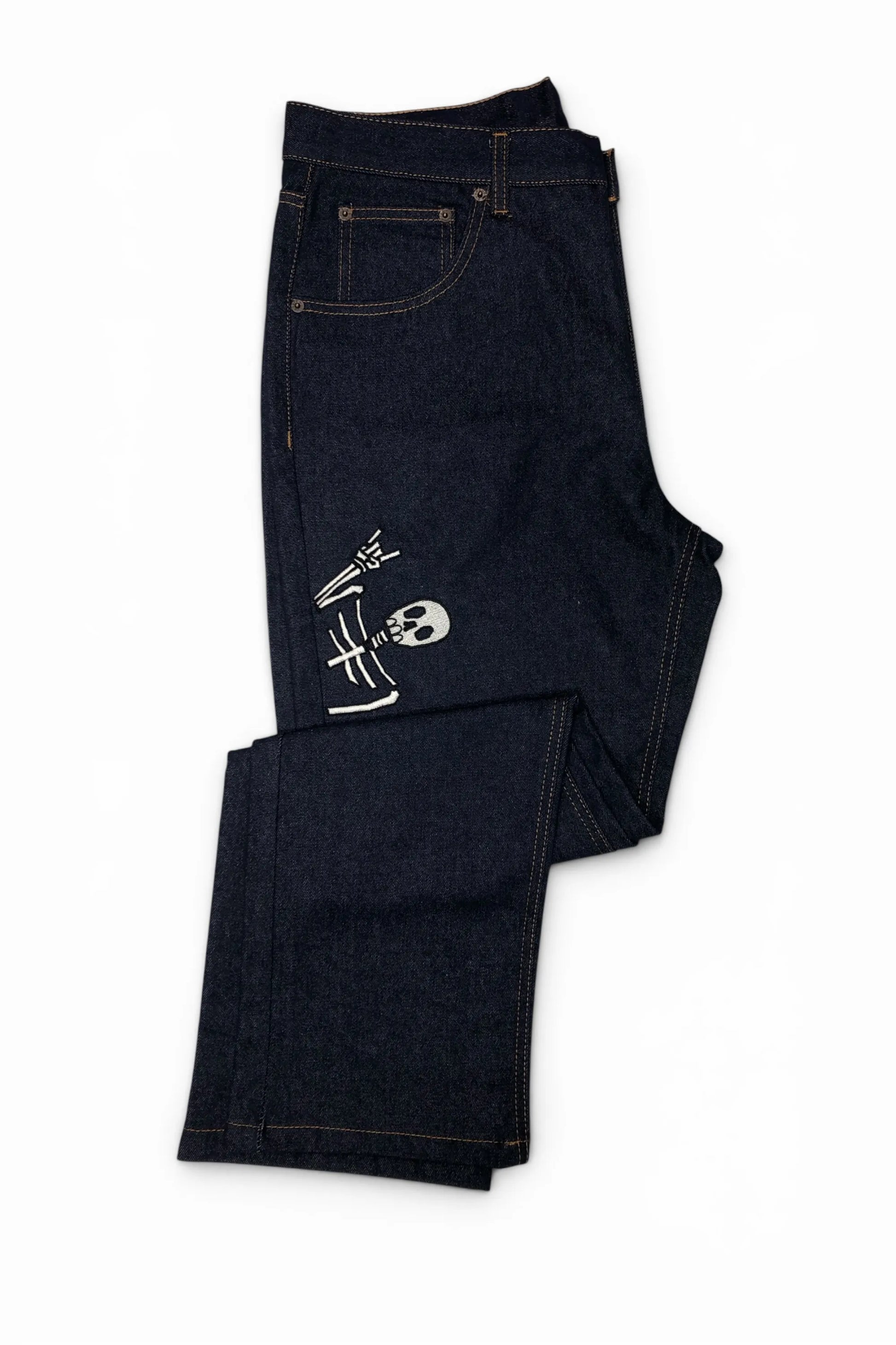 Common Saints dark indigo denim jeans with contrast stitching and white embroidered skull-and-bones graphic on the left thigh, folded view