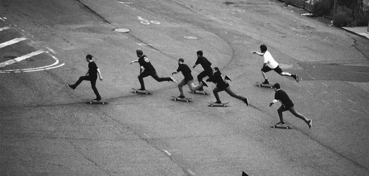 Black and white photo of multiple skateboarders in motion on a street.